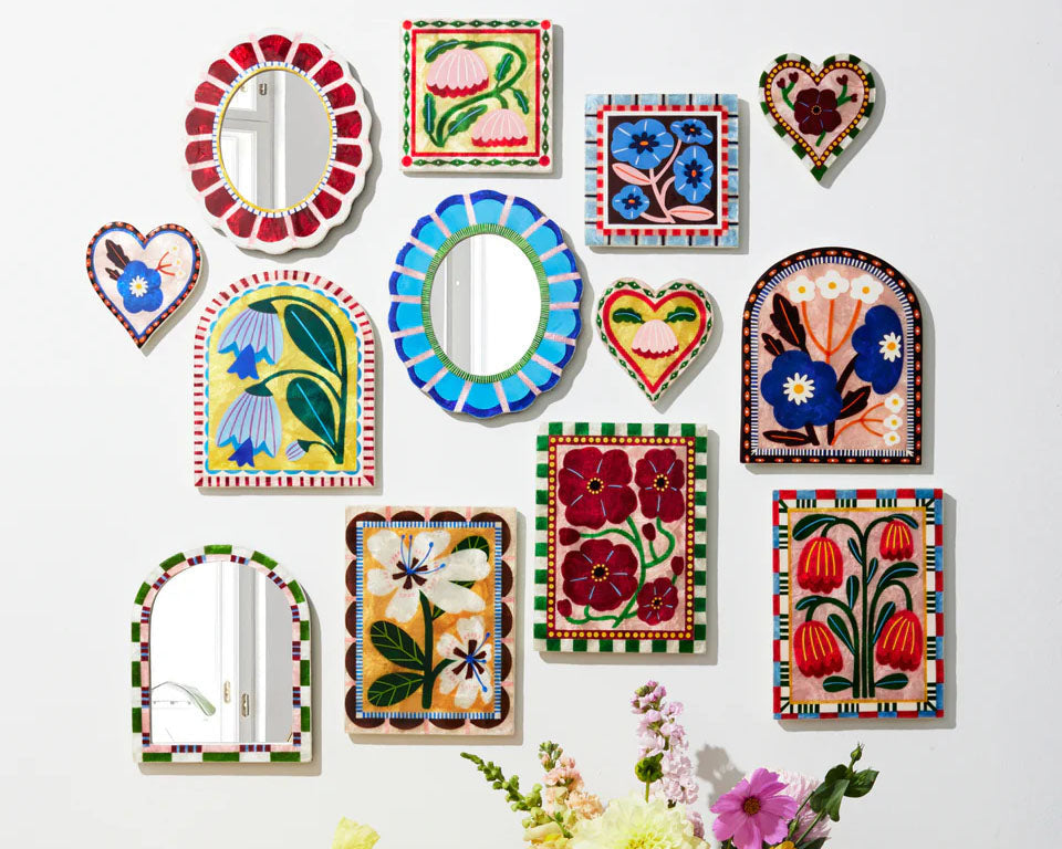 Collection of colorful decorative tiles and mirrors on a white wall with floral arrangements.